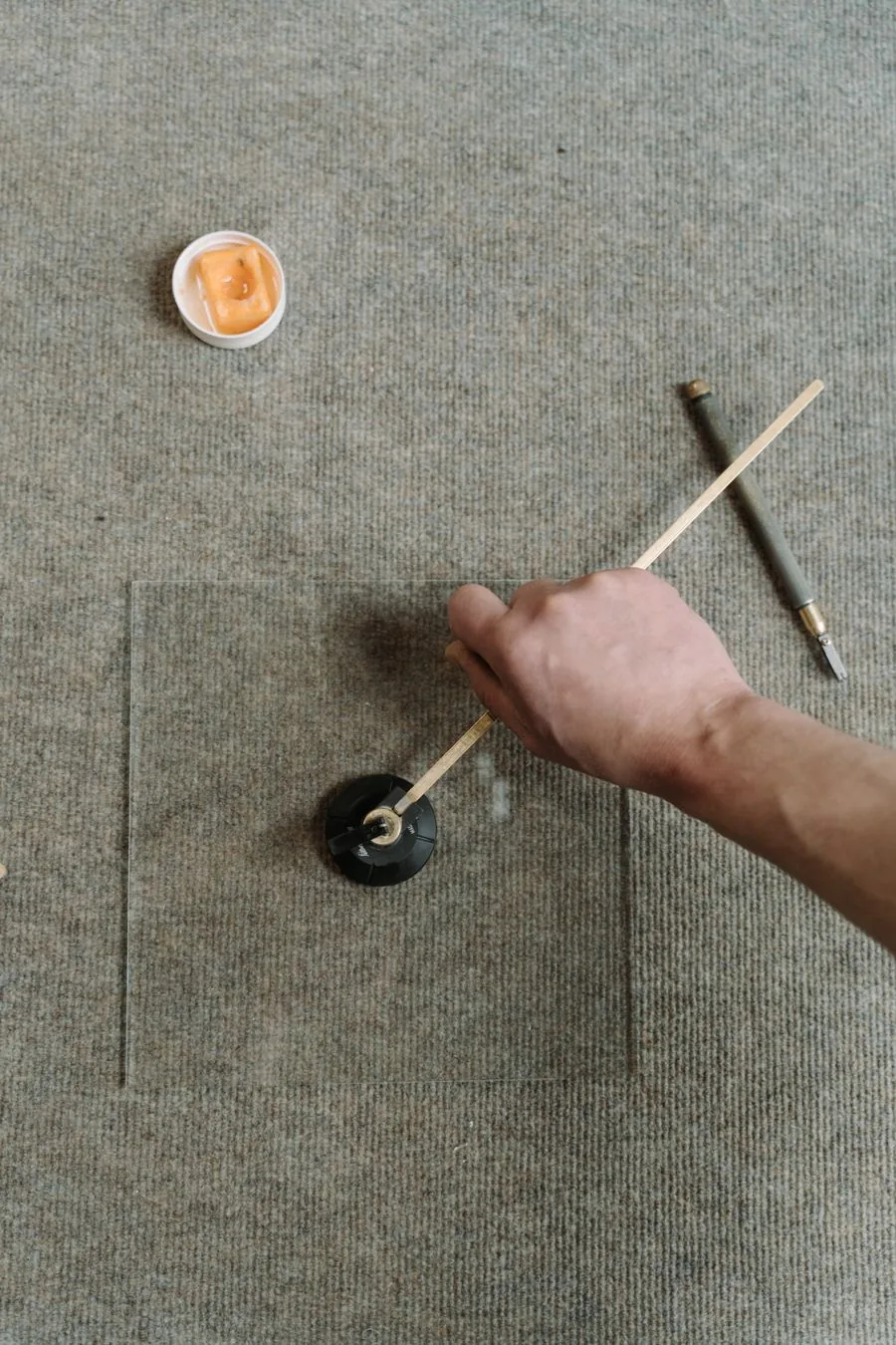 Glass sheet being cut with a hand-held circle cutter on a workbench