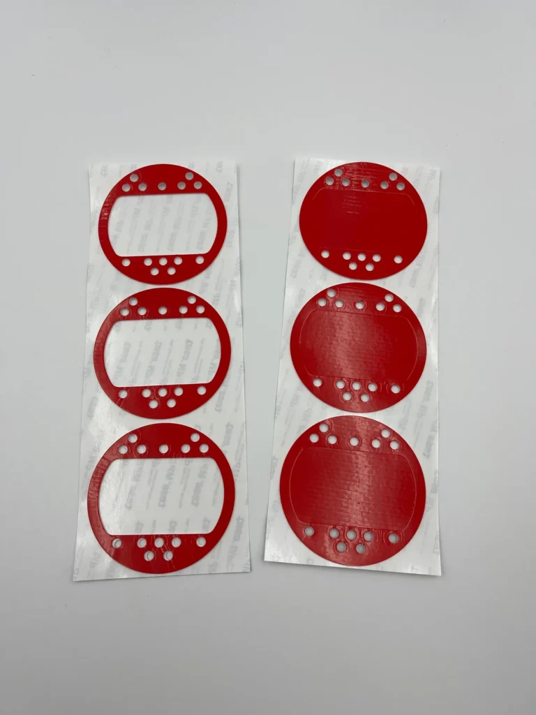 Actual red-liner die-cut adhesive parts with circular holes and shaped openings